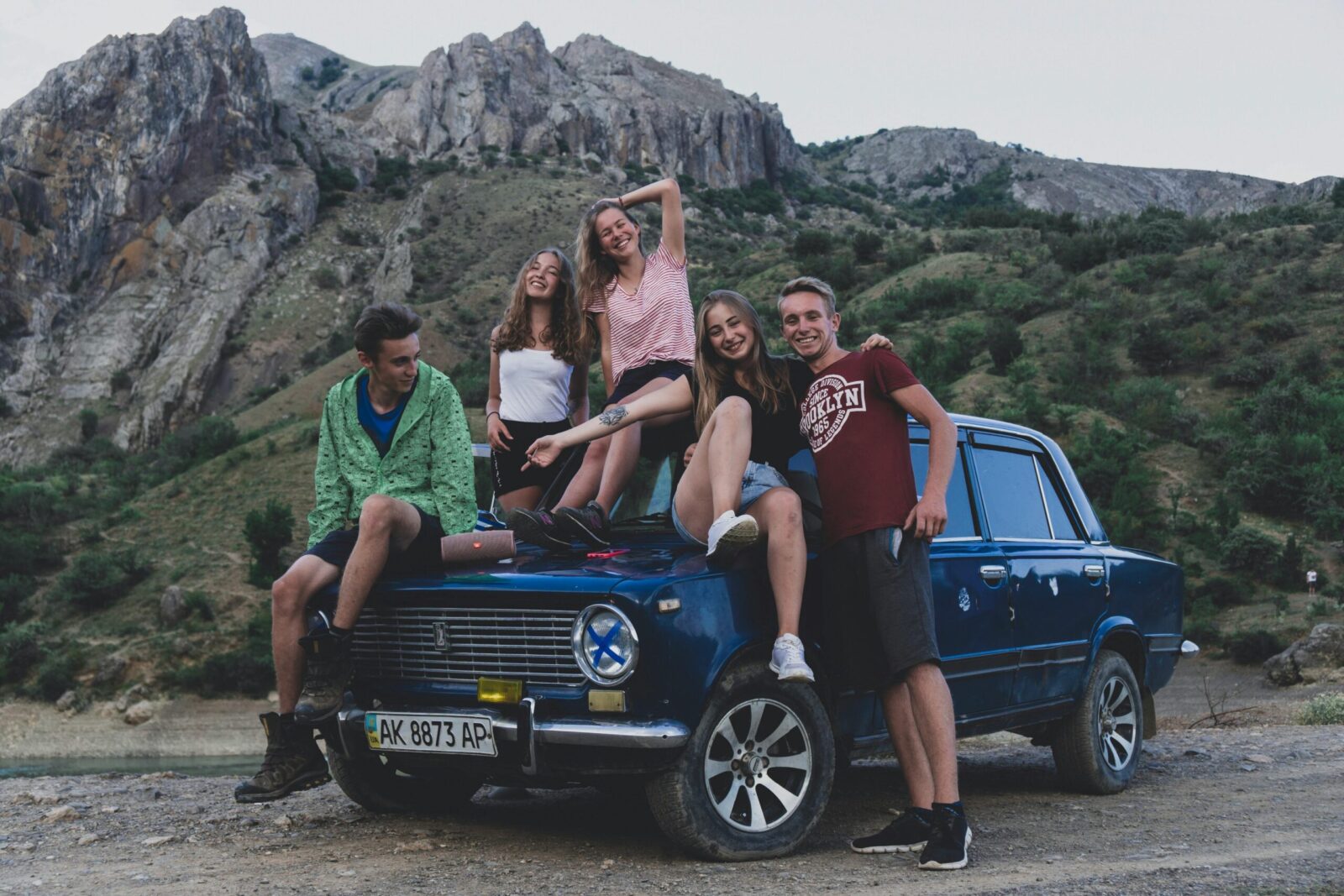 Group of friends sitting on a classic car in the mountains, enjoying a road trip adventure.