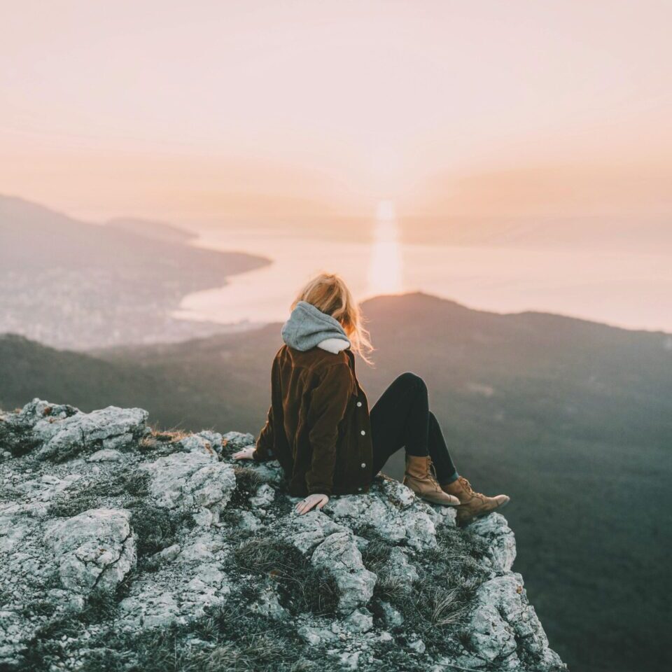 A woman sits on a rocky mountain enjoying the breathtaking sunrise view over the ocean.